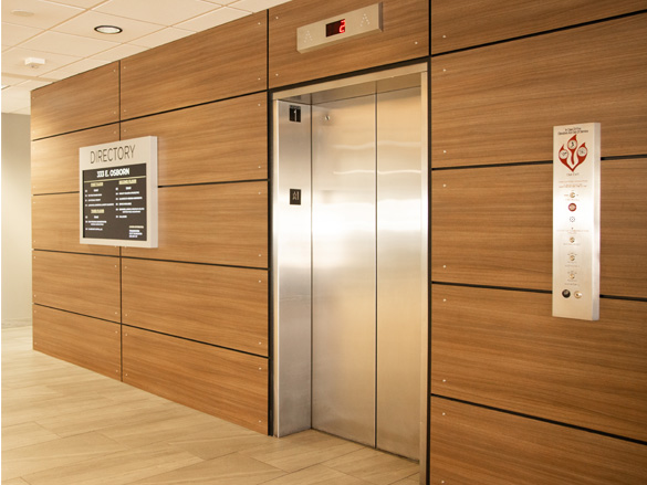 a hallway featuring wood-paneled walls, a directory sign, and clear safety signage next to a new elevator